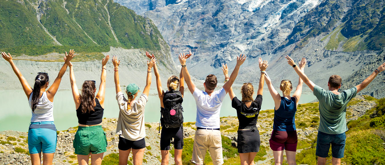 A group of hikers with raised arms celebrates the stunning glacial valley views in Aoraki Mount Cook National Park.