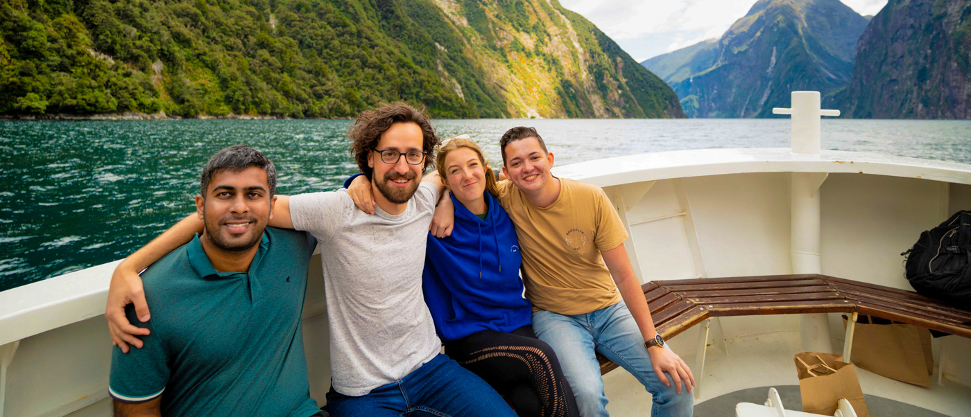 Four happy friends on a boat cruise through the towering cliffs of Milford Sound, New Zealand.