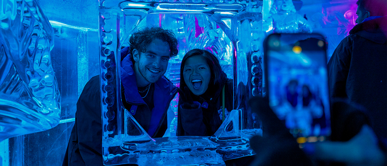 Two happy friends pose in an ice frame at a vibrant ice bar in Queenstown.