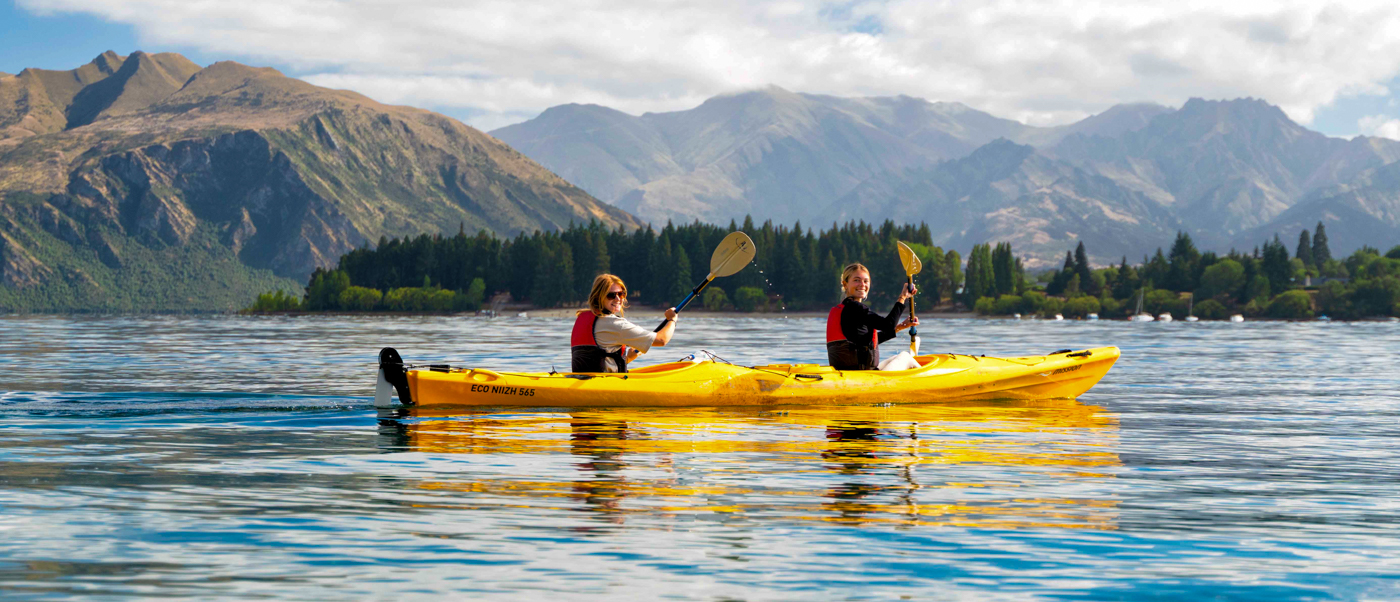 Two people kayaking on lake Wanaka with majestic mountains in the background.