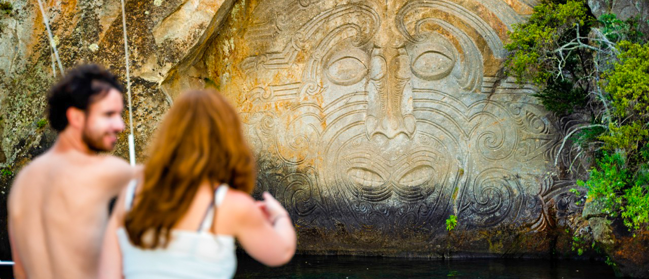 A couple on a boat admiring the large Māori rock carvings rising from Lake Taupo.