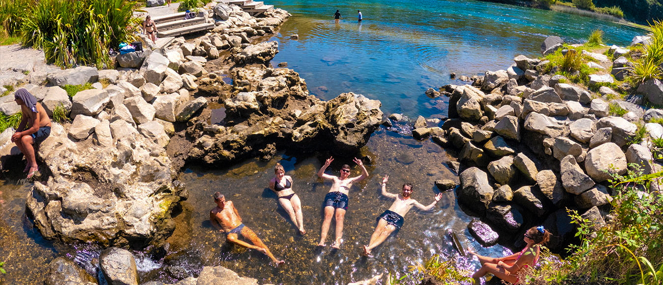 A group of friends happily relaxing in the clear, warm waters of natural hot springs in Taupo.