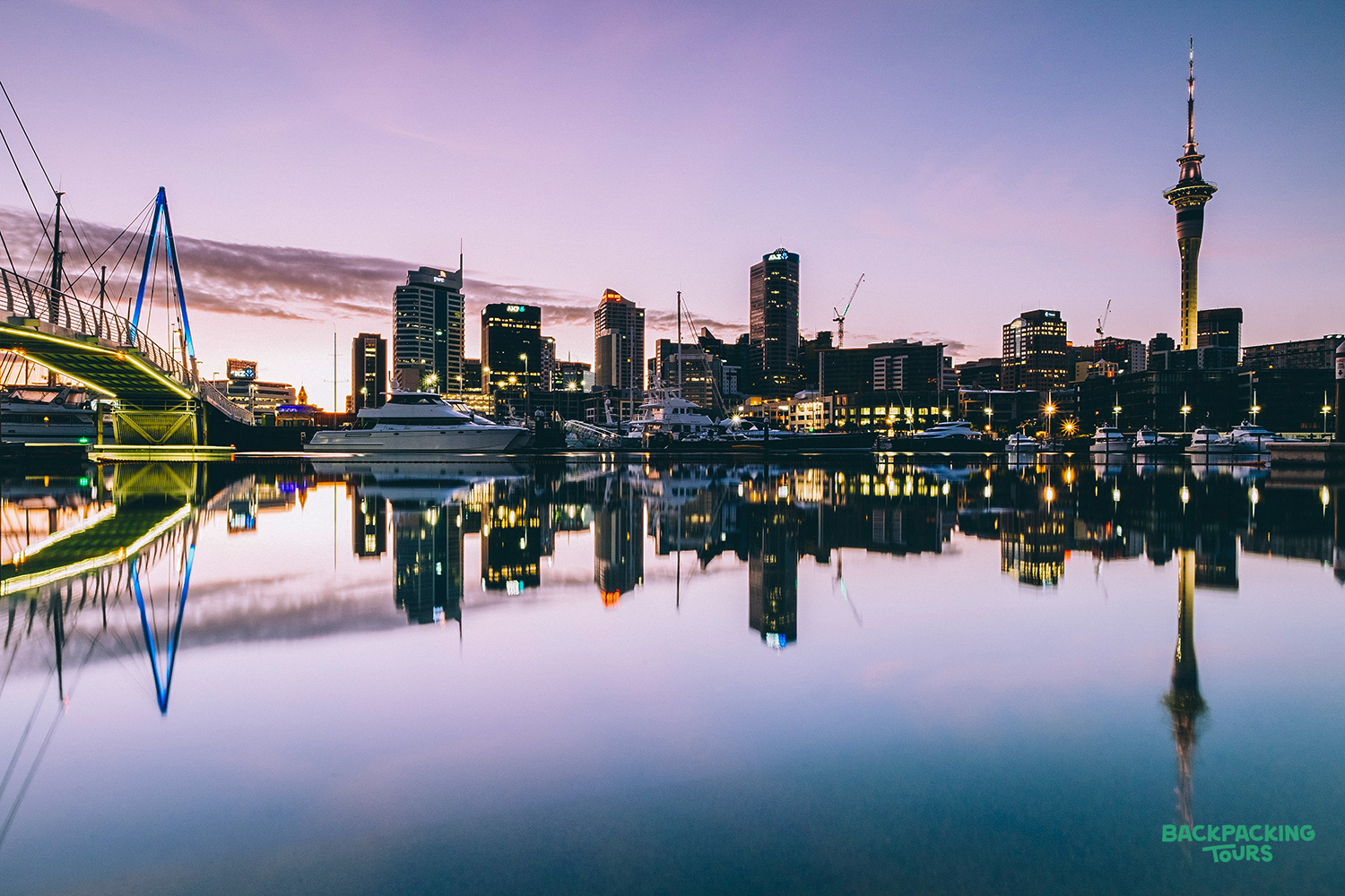 Auckland's vibrant city skyline at twilight, featuring the iconic Sky Tower, harbor, and stunning water reflections.