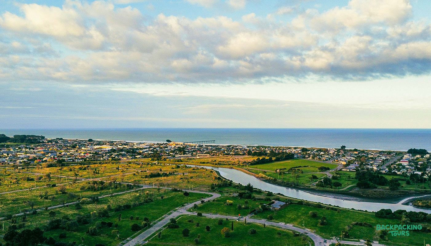Coastal city of Christchurch from above, with a river meandering through green landscapes to the ocean.