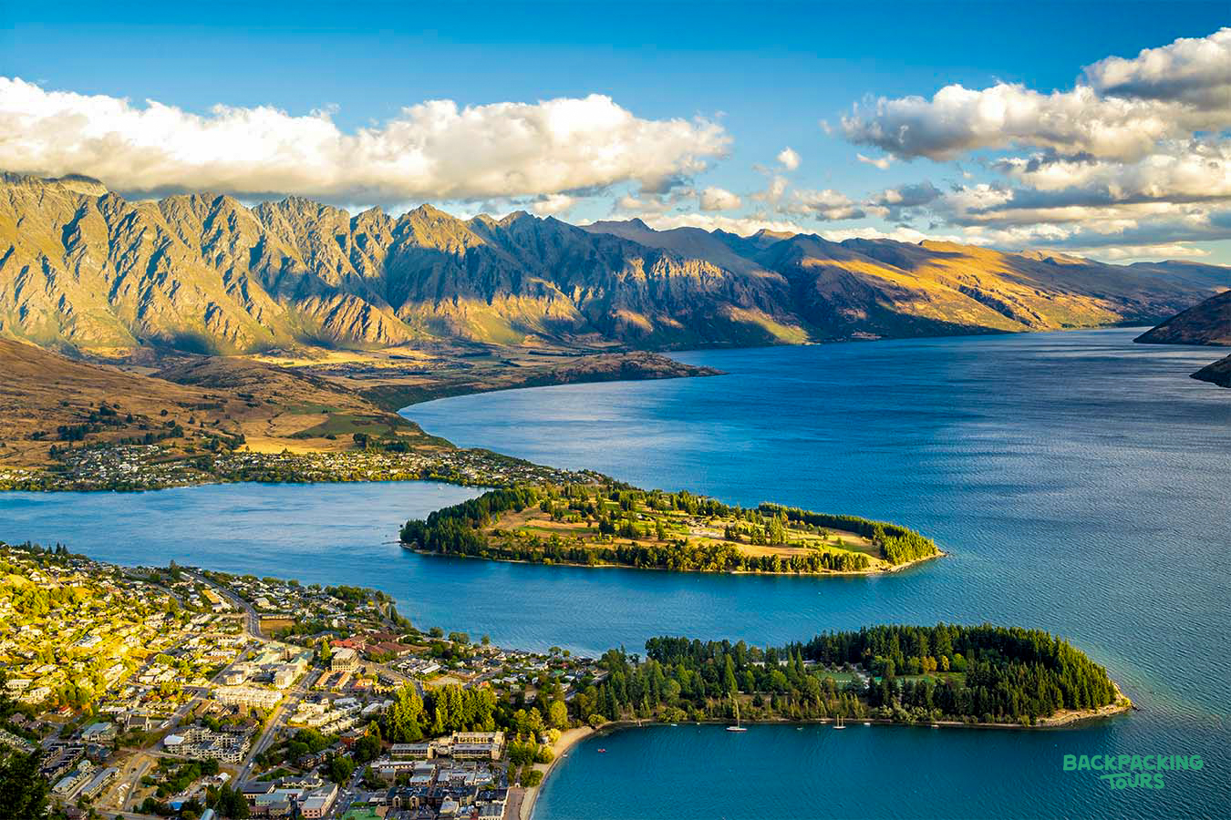 Panoramic view of Queenstown, New Zealand, with its vibrant town, deep blue lake, and majestic mountains.