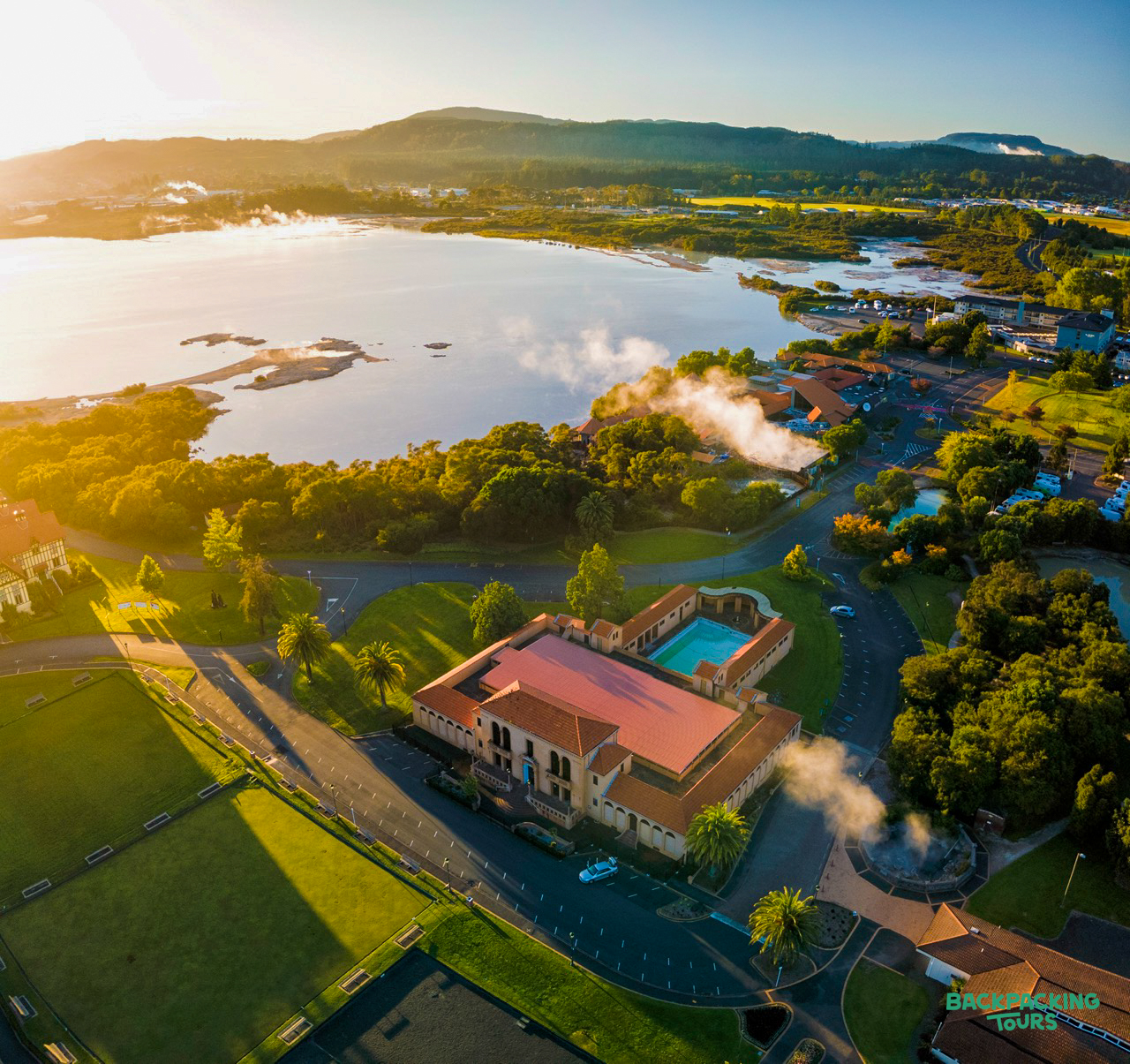 Rotorua's historic bathhouse and steaming lake at golden hour, showcasing New Zealand's geothermal wonders.
