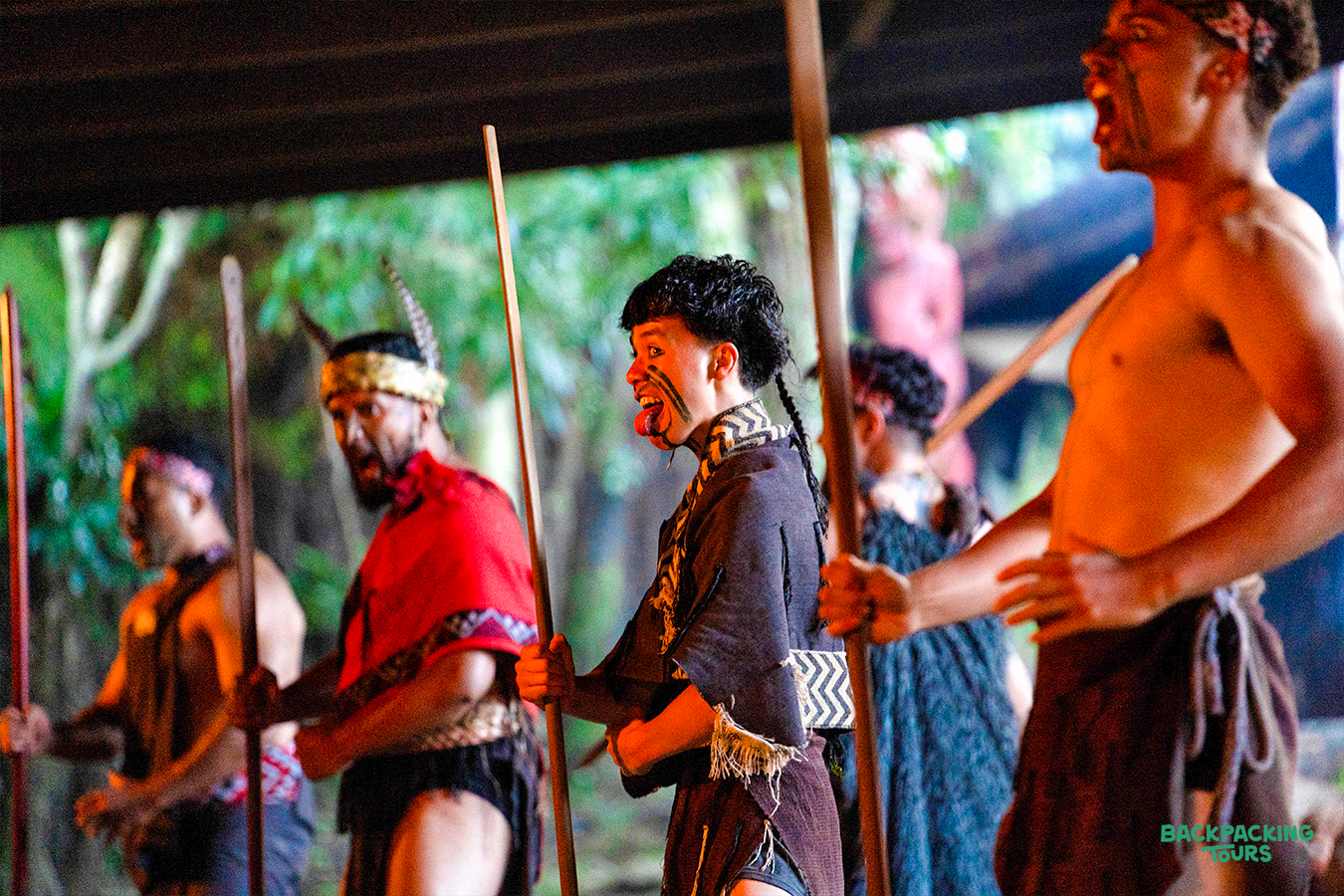 Māori performers in traditional dress with staffs, making expressive faces during a haka in Rotorua.