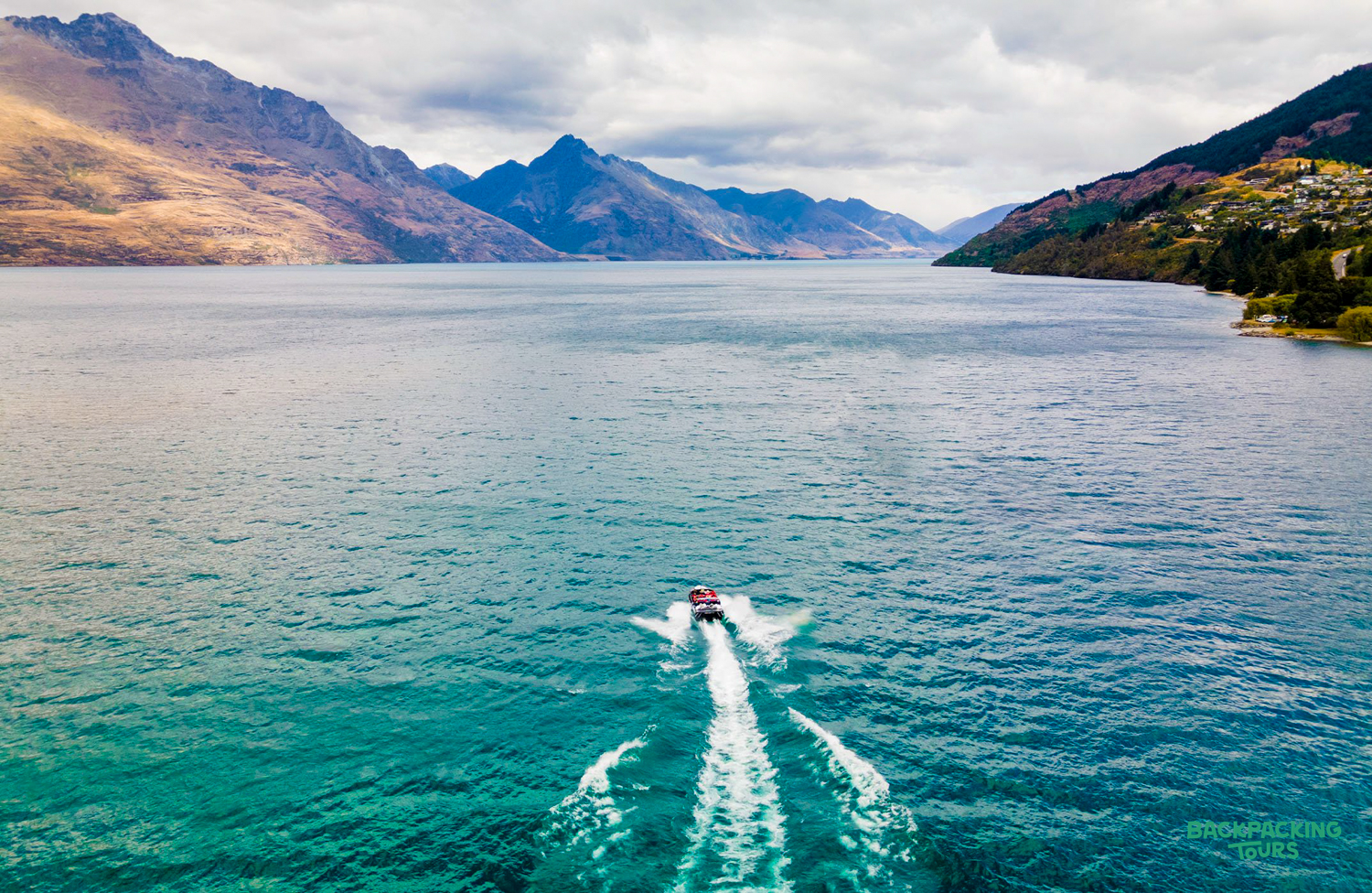 A jet boat speeds across the stunning blue waters of Lake Wakatipu, Queenstown, surrounded by majestic mountains.