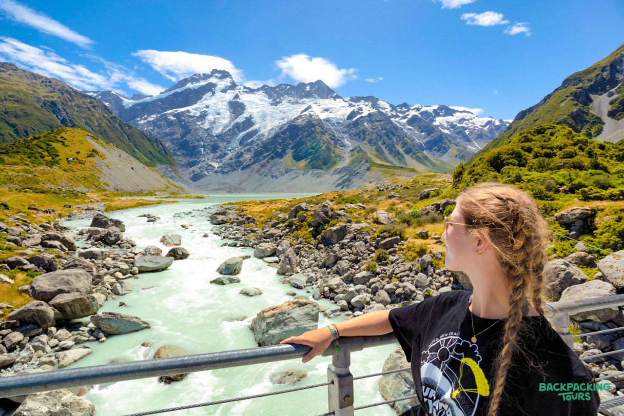 A woman gazes at the glacial river and snow-capped peaks of Mount Cook National Park, New Zealand.