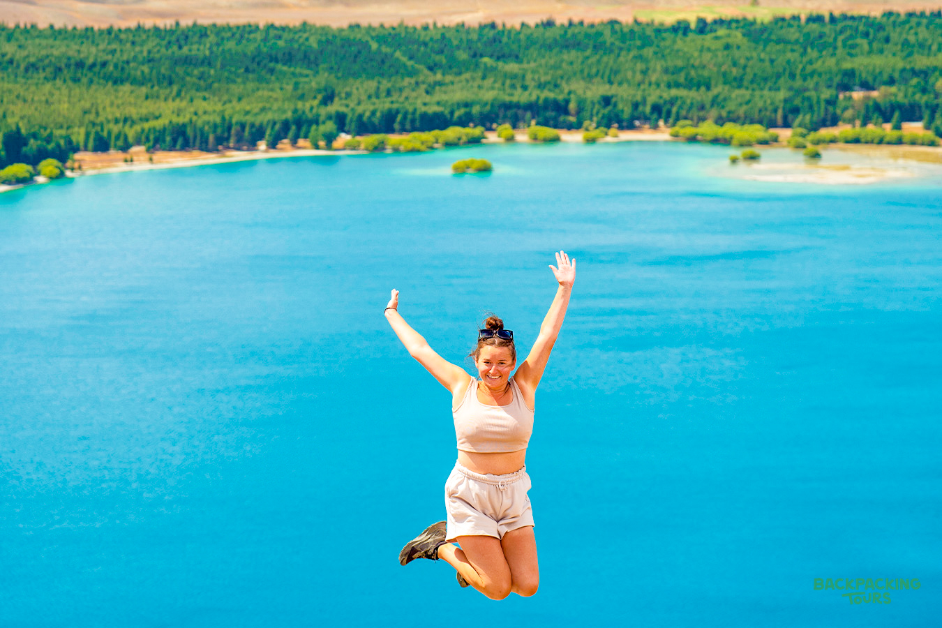 A joyful woman jumps high above the stunning turquoise waters of Lake Tekapo, New Zealand.