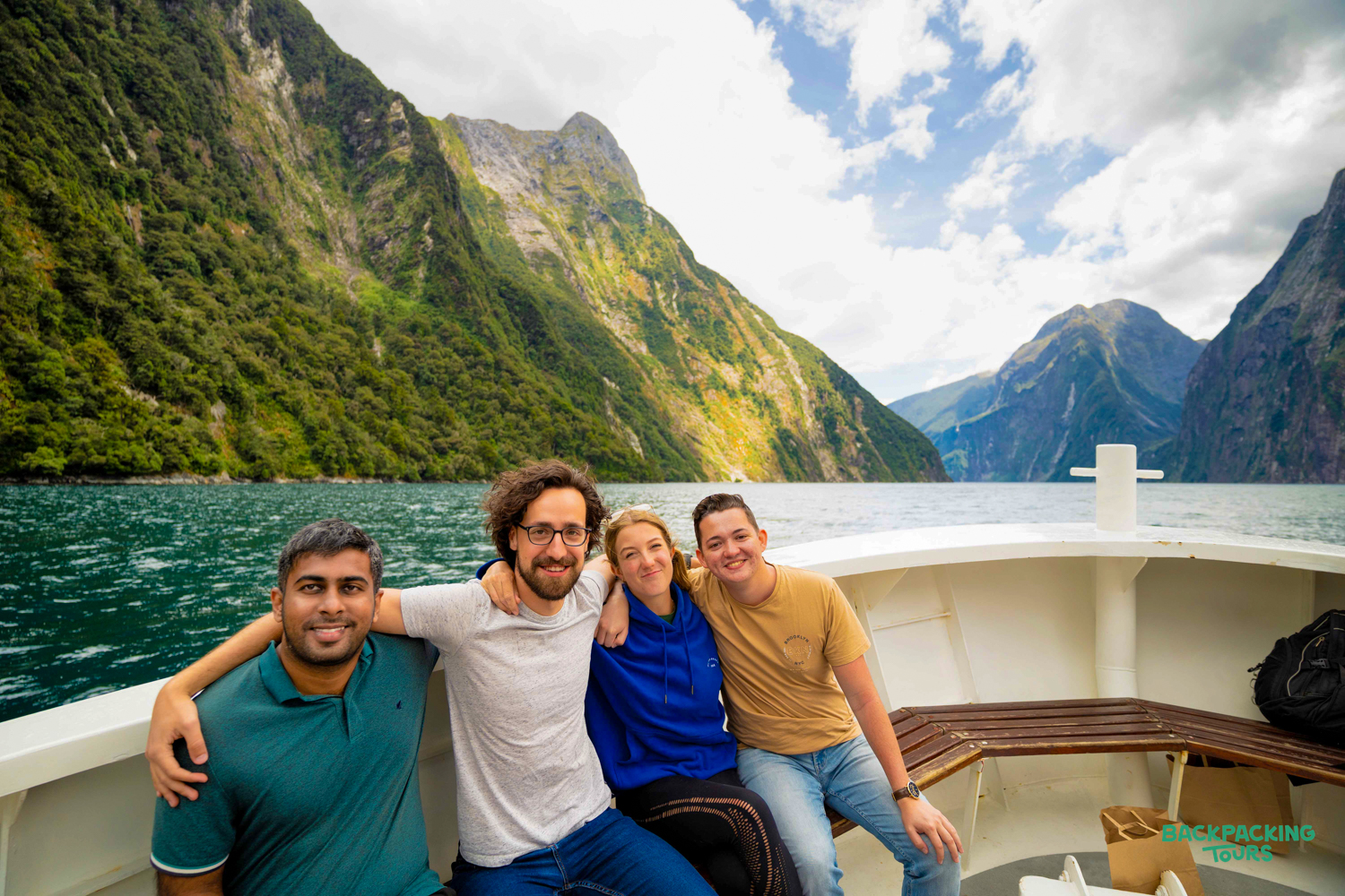 Four smiling friends enjoy a scenic boat cruise through the majestic Milford Sound fiords.