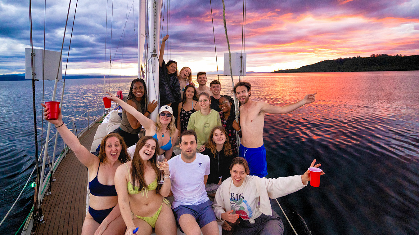 Happy group of friends on a boat enjoying a vibrant sunset over Lake Taupo, New Zealand.