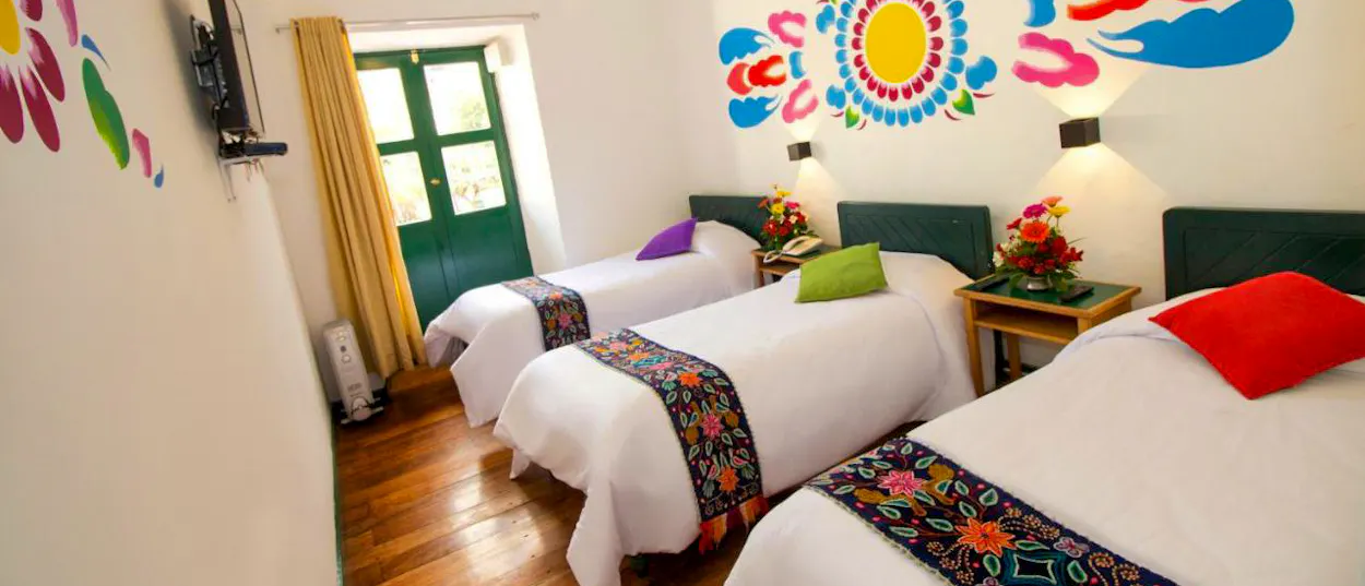 A vibrant hotel room in Cusco, Peru, featuring three beds with colorful runners and wall murals.