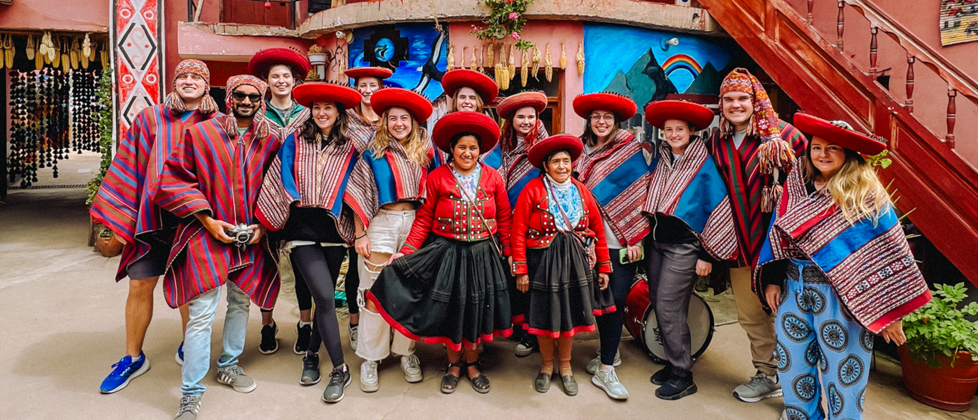 A group of smiling tourists and local women in traditional Peruvian attire in Cusco.