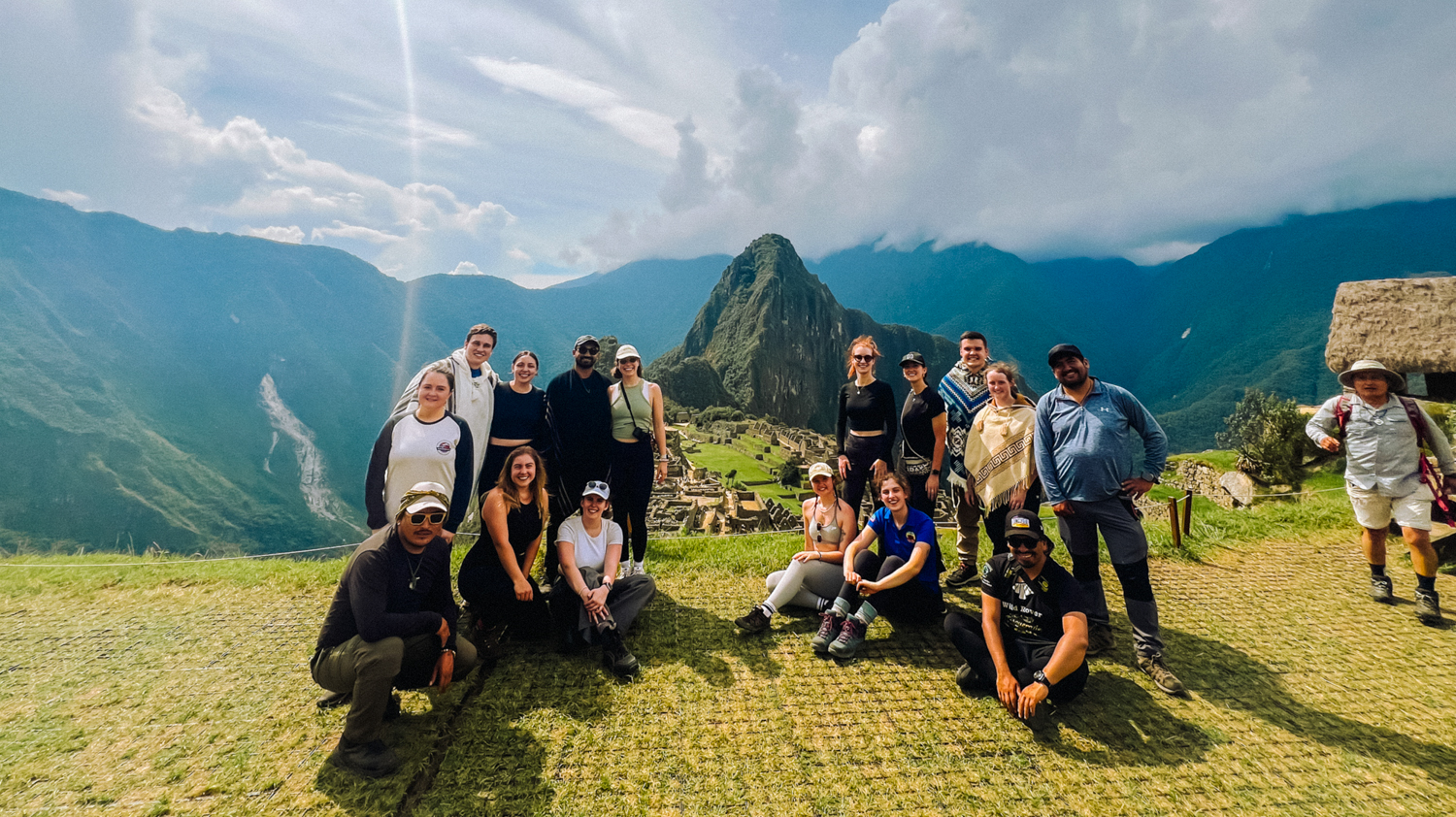 A diverse group of happy travelers posing for a photo with the majestic Machu Picchu mountains.