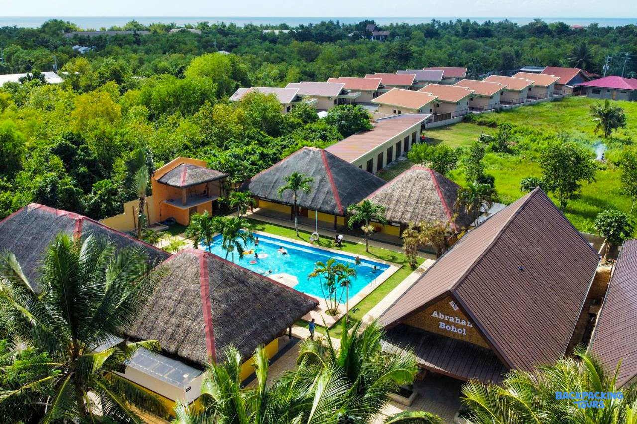 Guests enjoying the swimming pool at Abraham Bohol resort, surrounded by tropical foliage and buildings.