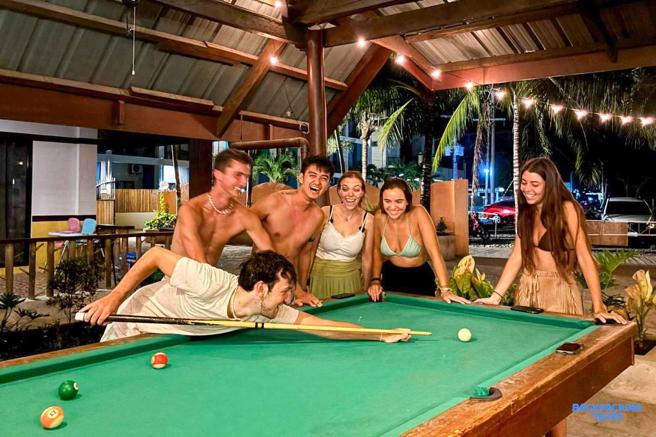 Five young friends enjoy a lively game of pool, laughing together under string lights in Bohol.