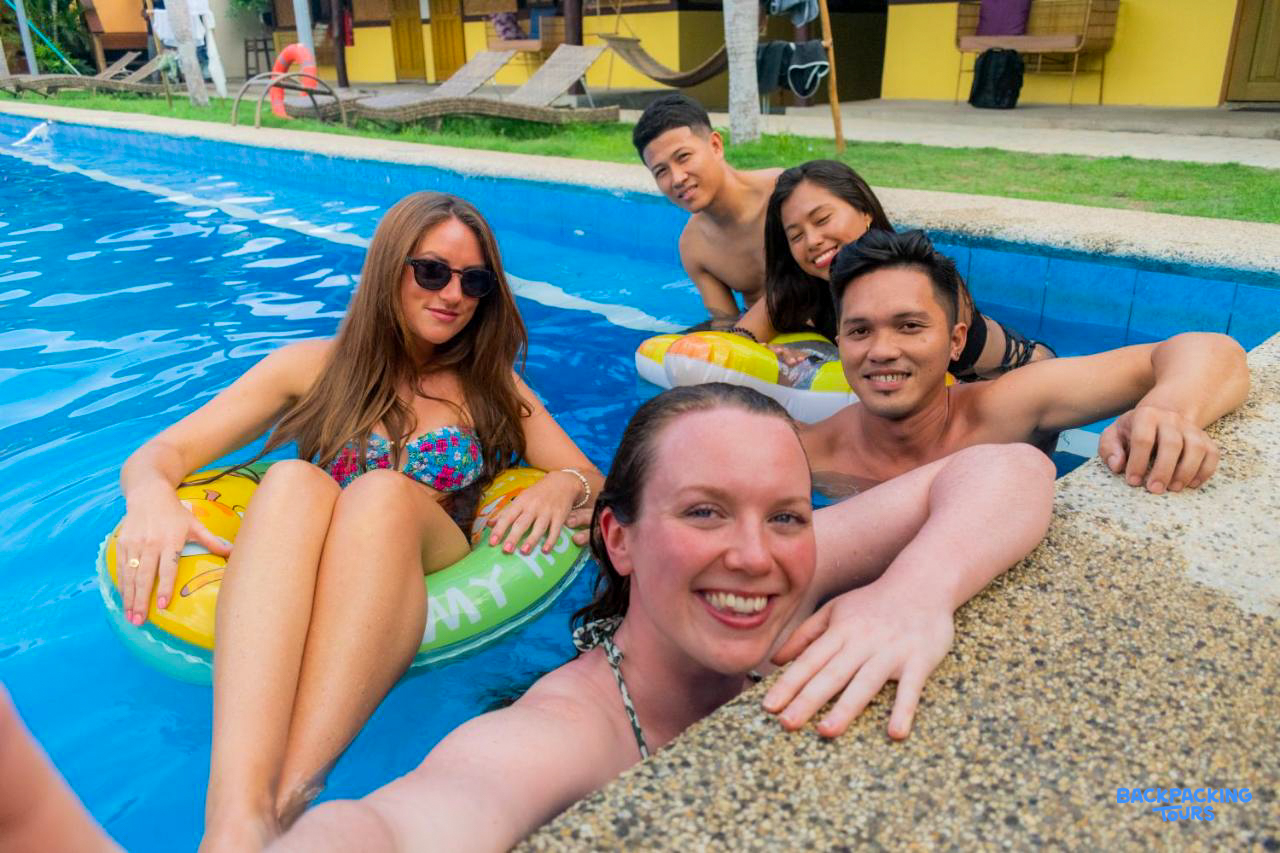 Happy backpackers relaxing and smiling in a swimming pool at their accommodation in Bohol.