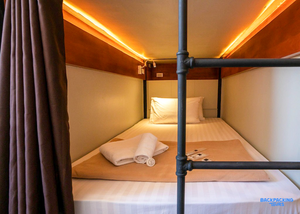 A cozy bunk bed with warm lighting and a privacy curtain in a Boracay hostel.