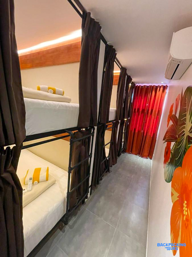 A modern hostel dorm room in Boracay featuring bunk beds with privacy curtains and tropical wall art.