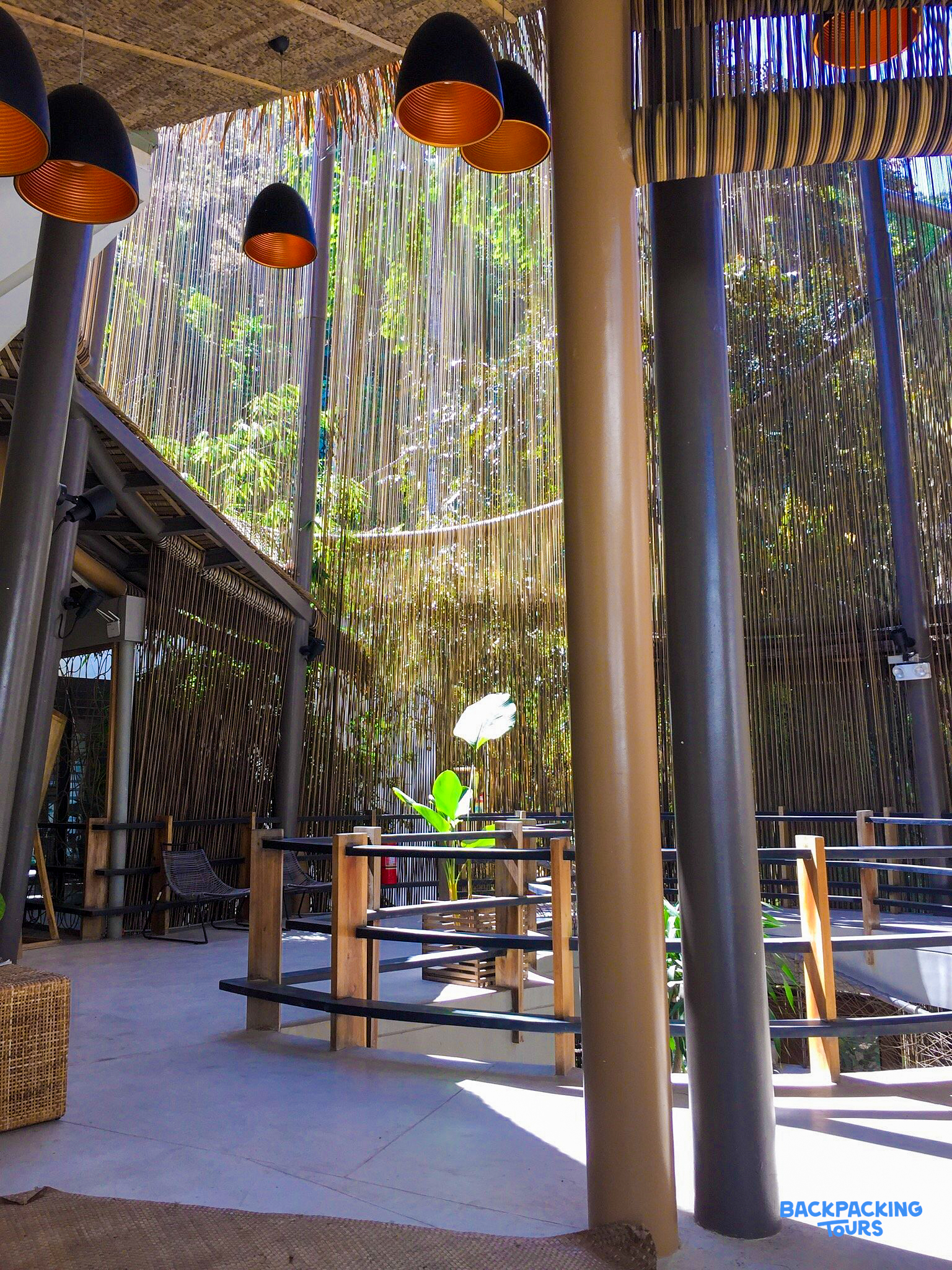 Stylish open-air lobby at a tropical hostel in El Nido, featuring modern lights and lush greenery.