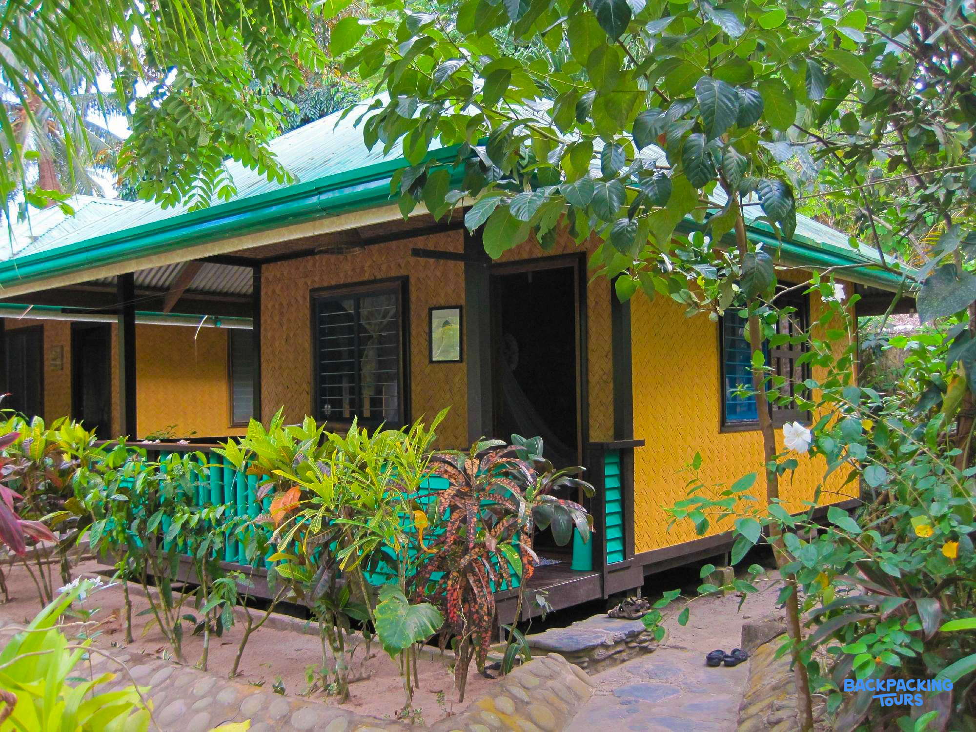 A charming yellow cottage with a green roof, surrounded by lush tropical plants in Port Barton.