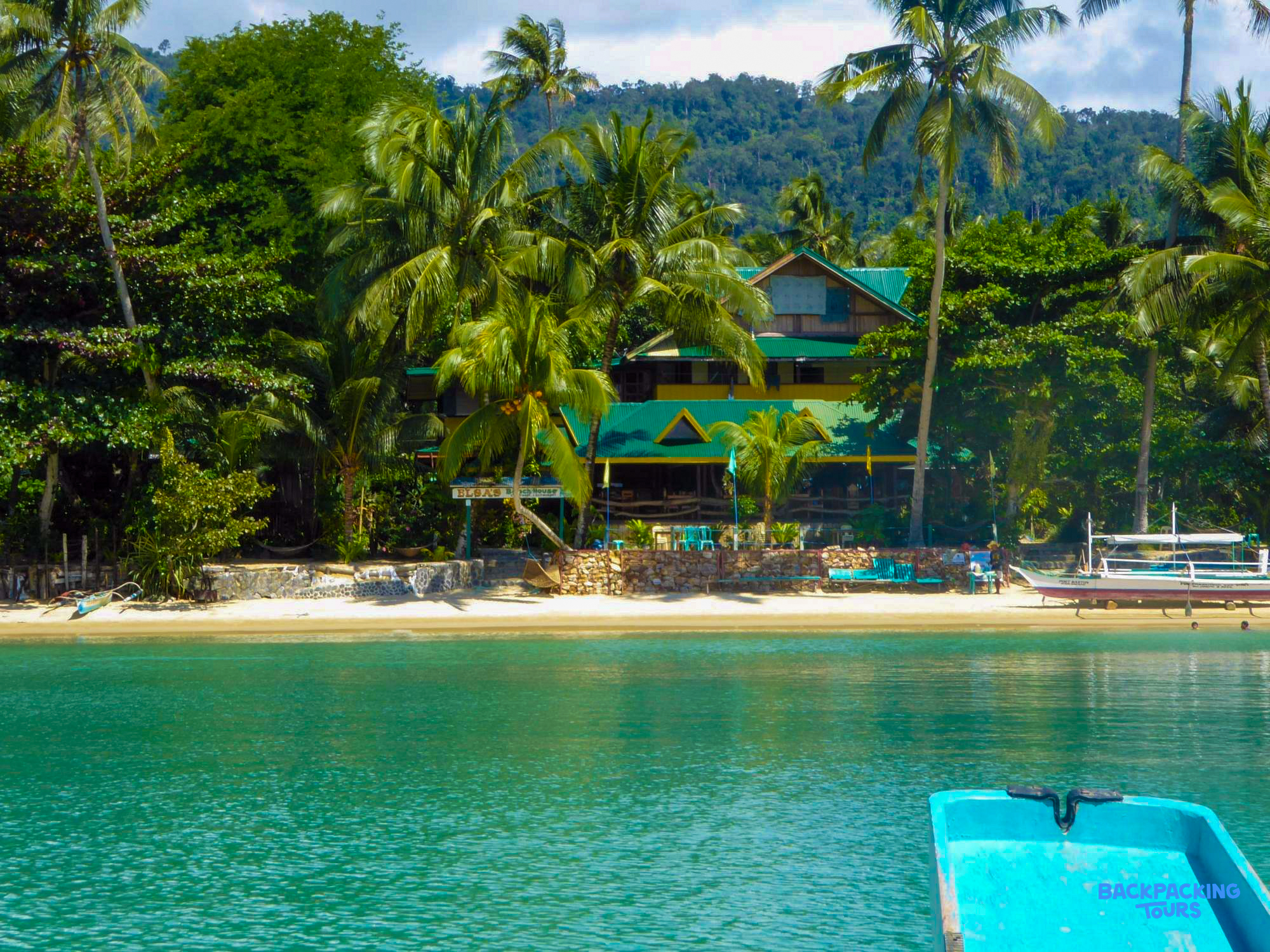 Elsa's Beach Cottages, a tropical resort with green roofs, golden sand, and clear turquoise water.