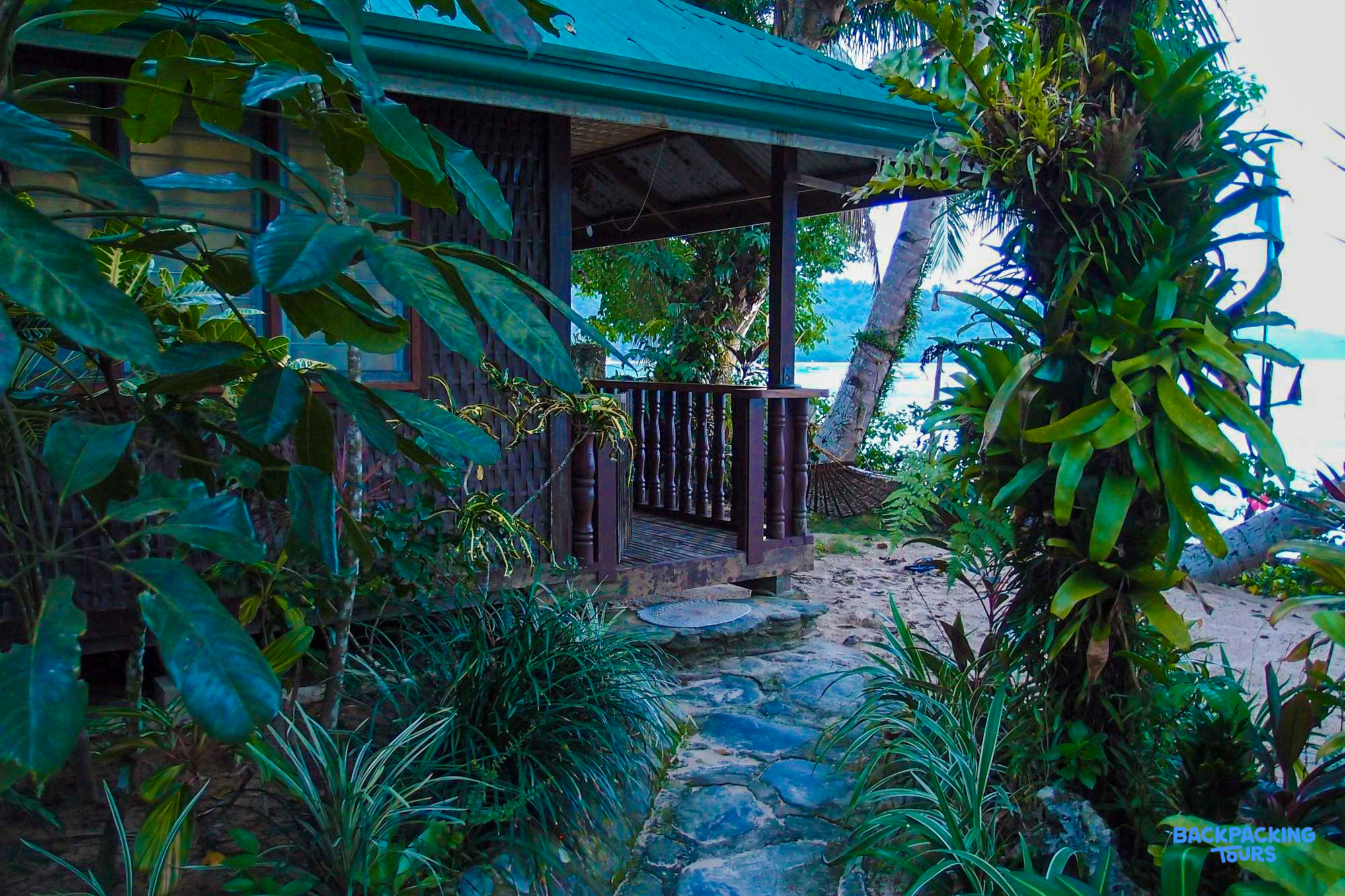 A charming tropical beach cottage with a green roof nestled among lush foliage in Palawan.