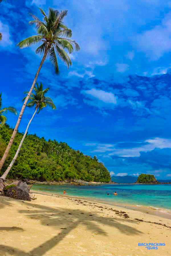 People enjoy swimming in the clear turquoise waters of a tropical beach in Port Barton.