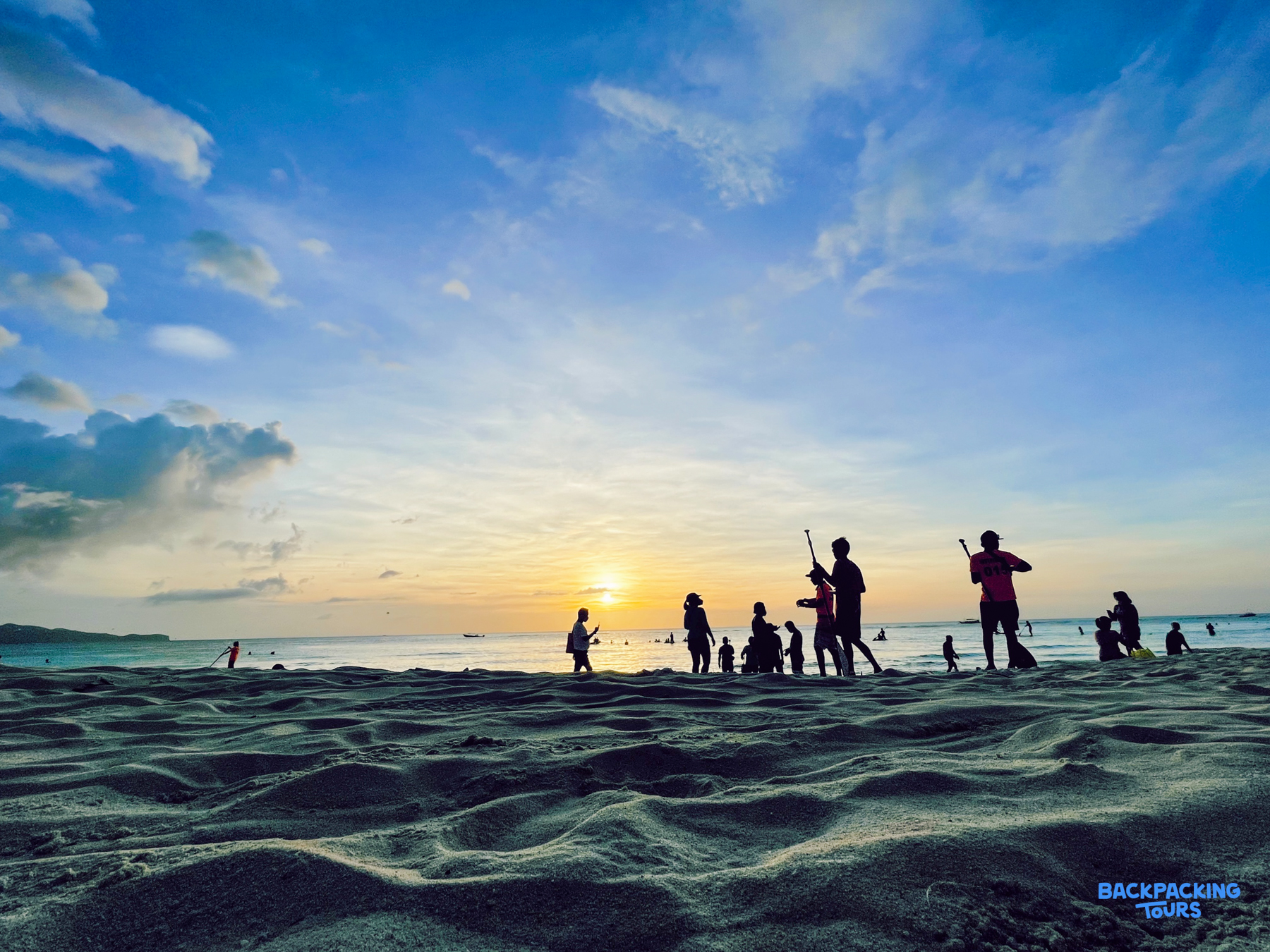 Silhouettes of people enjoying a beautiful sunset on a sandy beach in Boracay, Philippines.