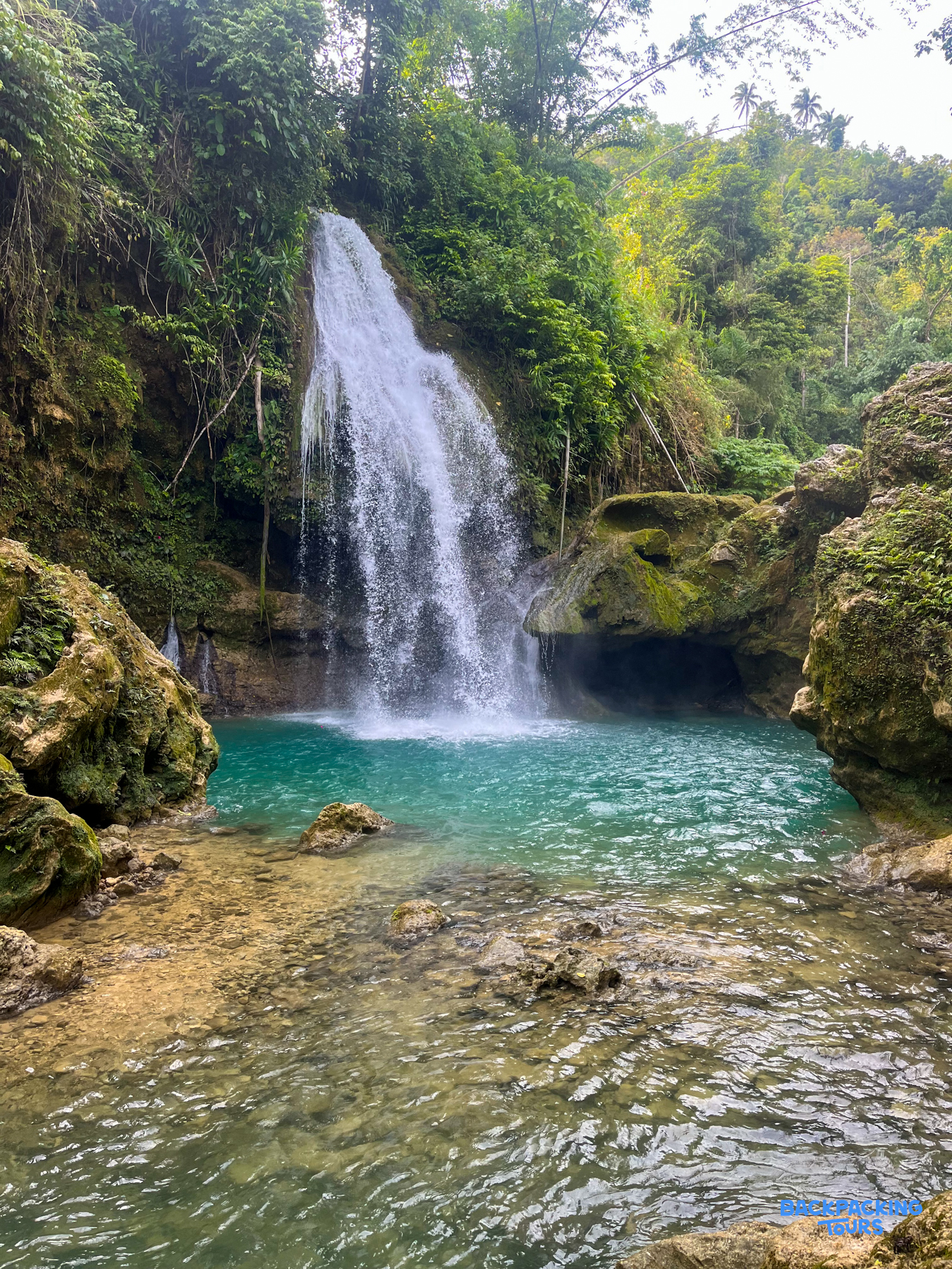Cambais Falls cascades into a vibrant turquoise swimming hole surrounded by lush green jungle.