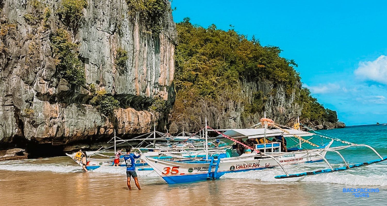 Traditional bangka boats on a sandy beach with towering limestone cliffs and clear blue water in El Nido.