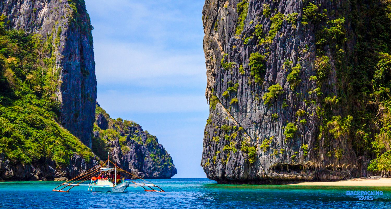 A traditional Filipino boat floats on clear blue water between towering limestone cliffs in Coron.