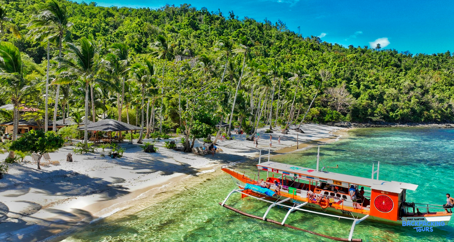 A vibrant outrigger boat on clear turquoise water by a white sand beach in Palawan.