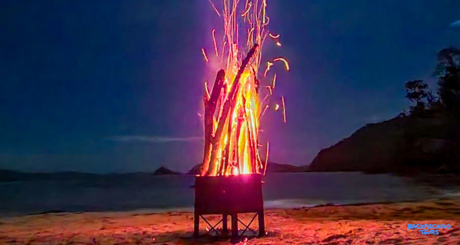 A glowing beach bonfire illuminates the night on a sandy shore at Island Camp.