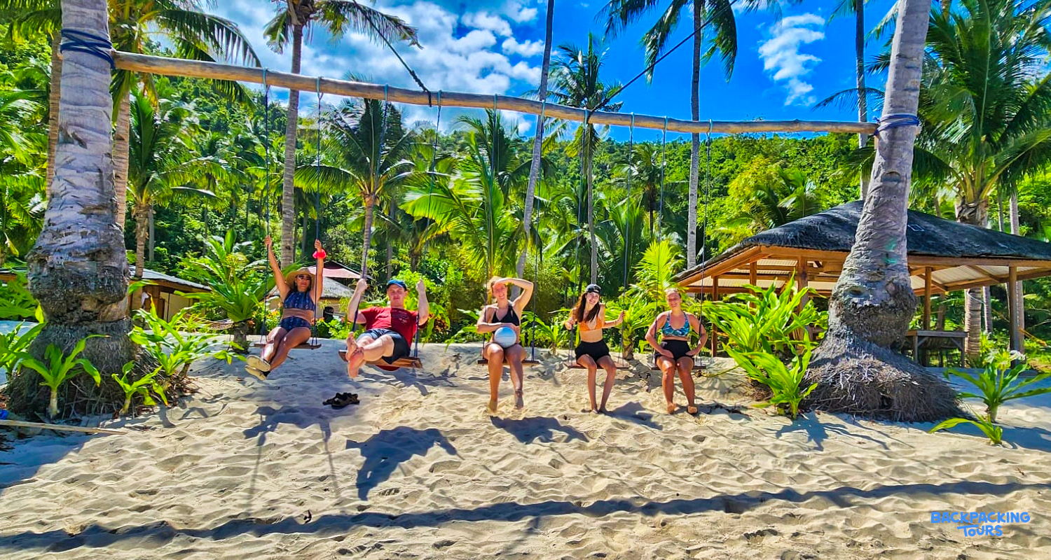Five backpackers enjoying a large swing on the sandy beach at Island Camp, Philippines.