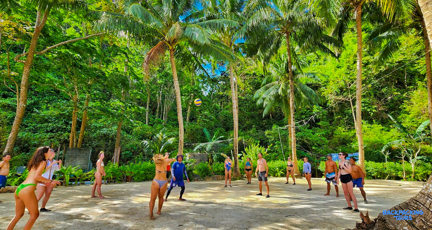 A group of backpackers plays volleyball under tall palm trees at Island Camp, Philippines.