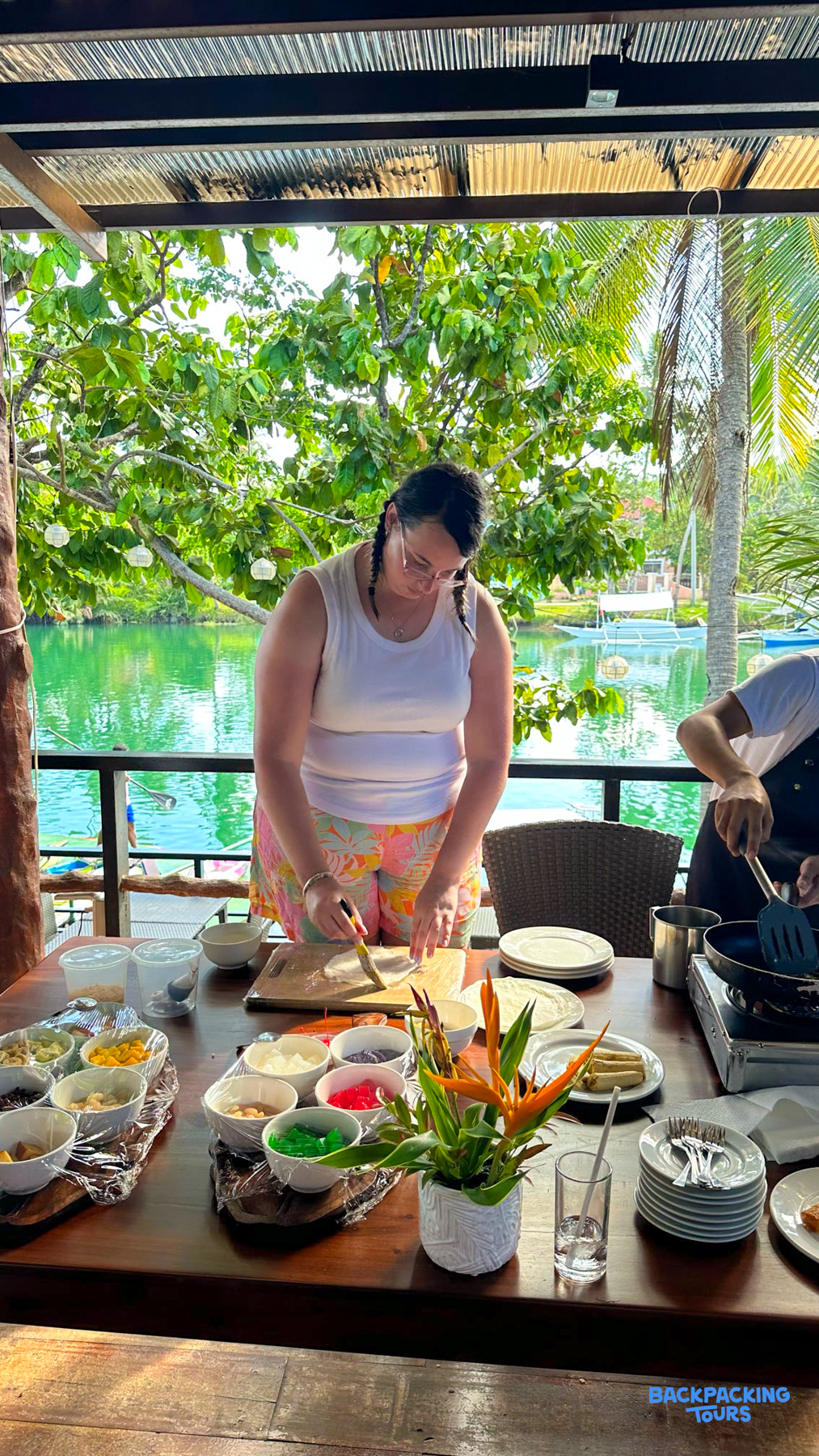 A participant enjoys a hands-on cooking class with colorful ingredients by the tropical Loboc River.
