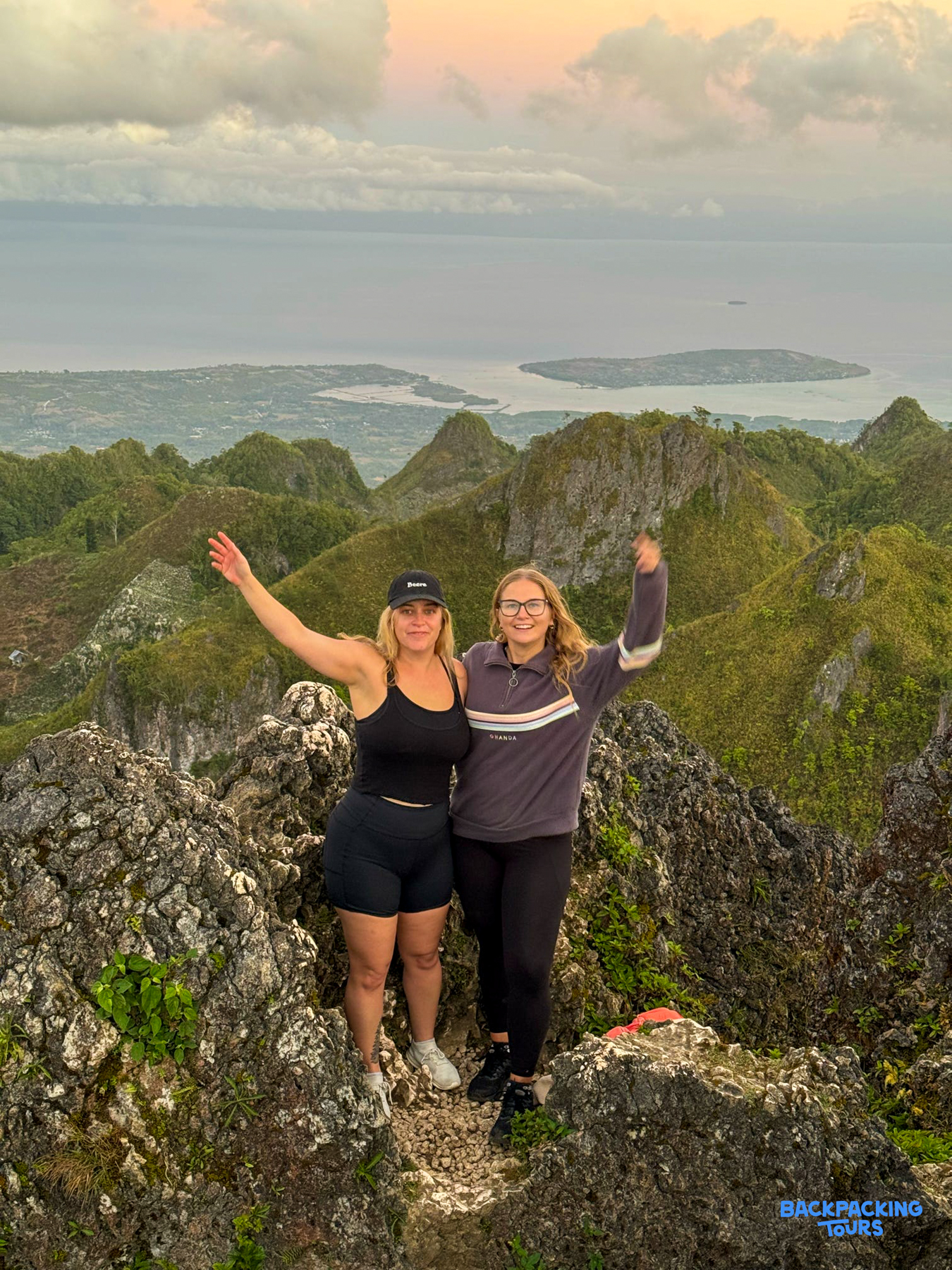 Two happy hikers at Osmena Peak during sunrise, with a panoramic view of Cebu's rugged landscape.