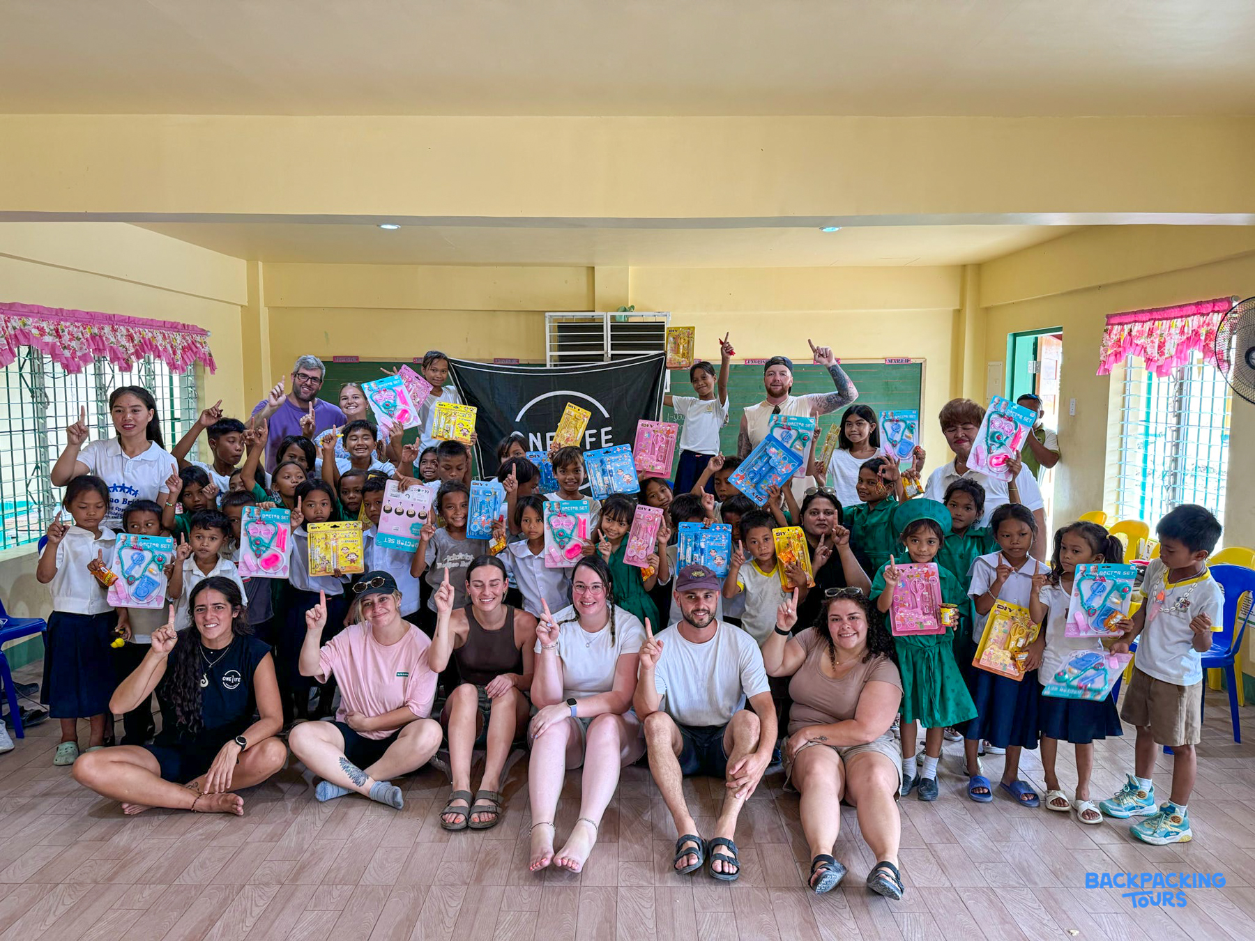 Joyful children and adults in Bohol celebrating a school visit, holding up their new gifts.
