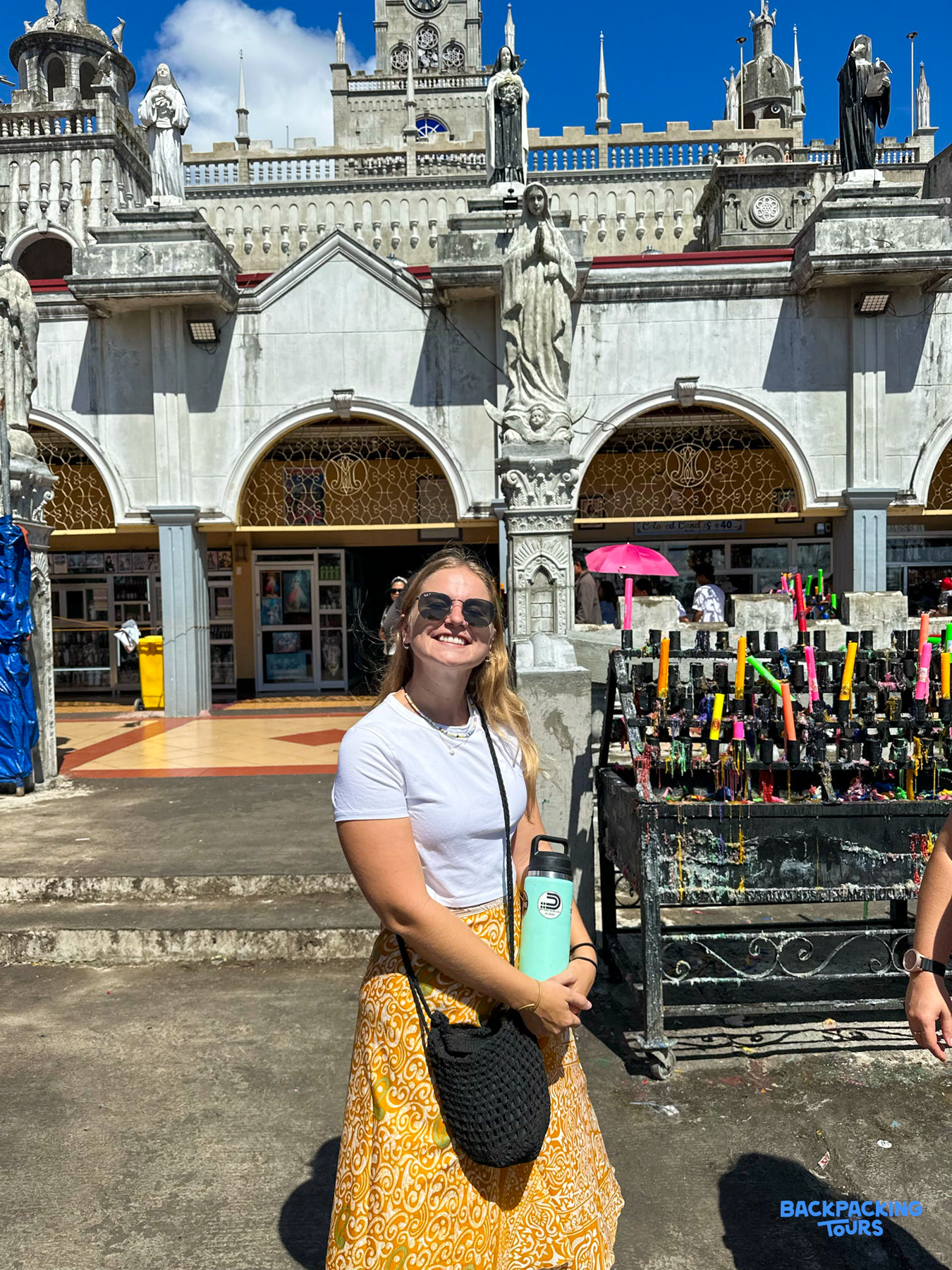 A smiling traveler stands before the ornate Simala Shrine with its many statues in Cebu.