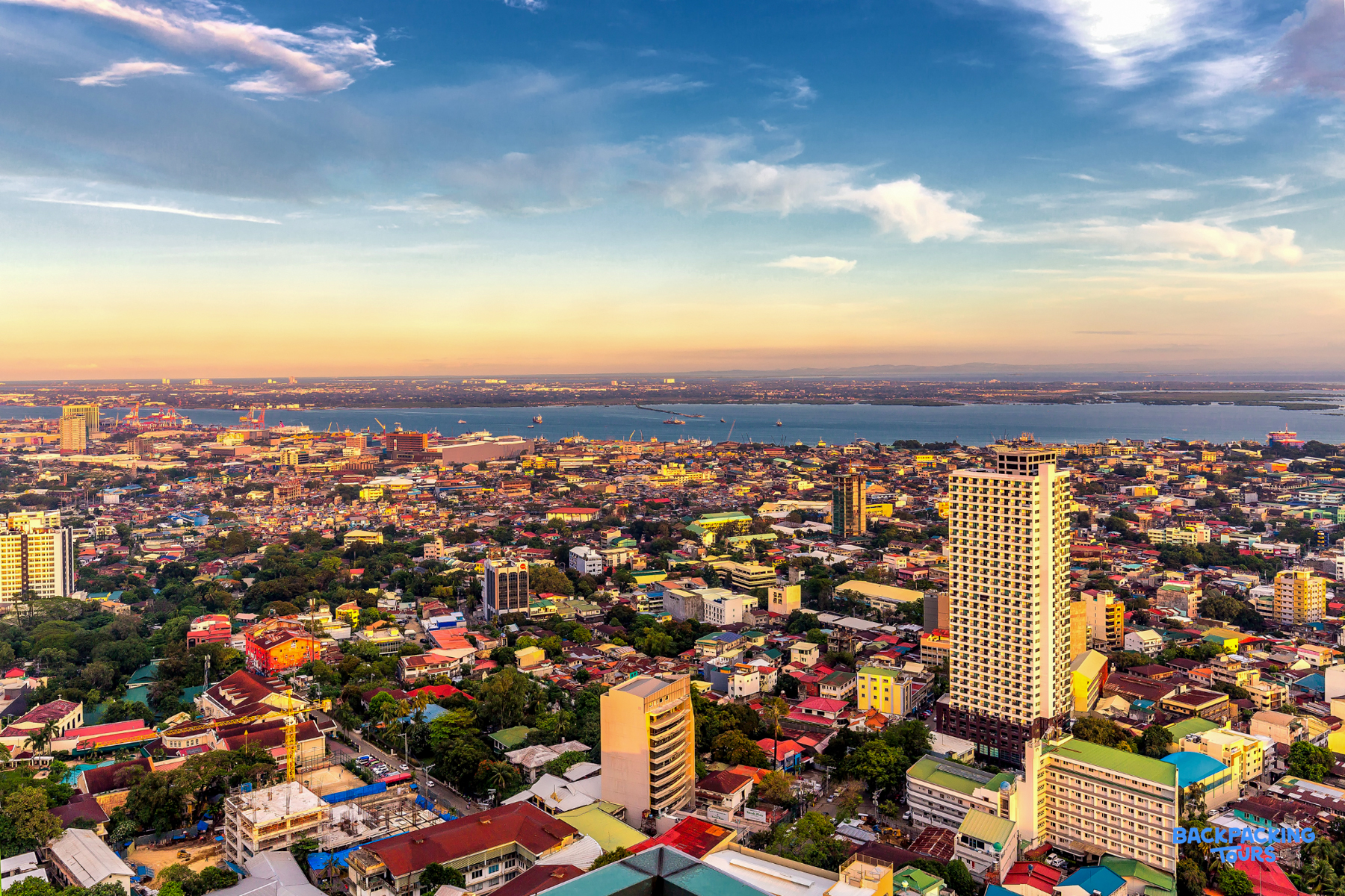 Panoramic view of vibrant Cebu City at sunset, showcasing diverse architecture and a wide bay.