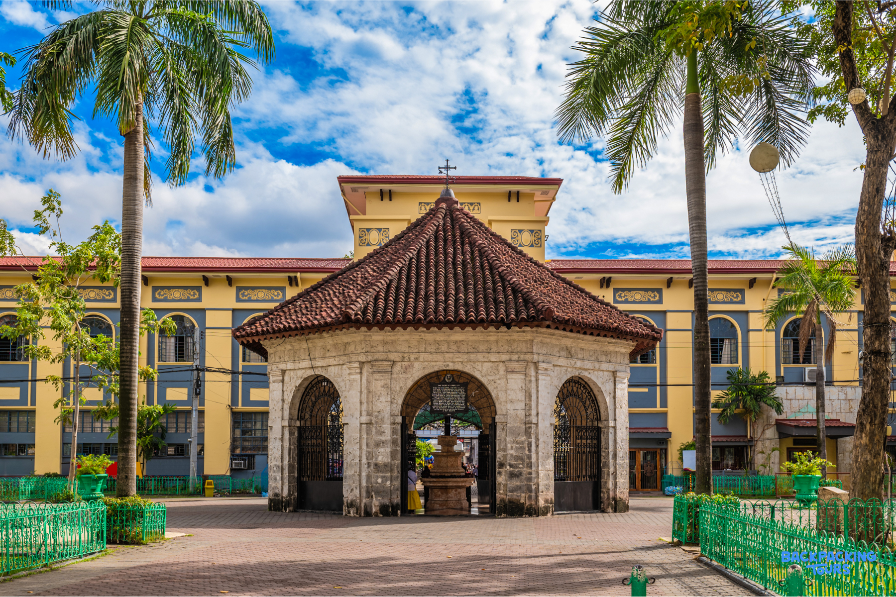 Magellan's Cross pavilion in Cebu City, framed by tall palm trees under a bright sky.