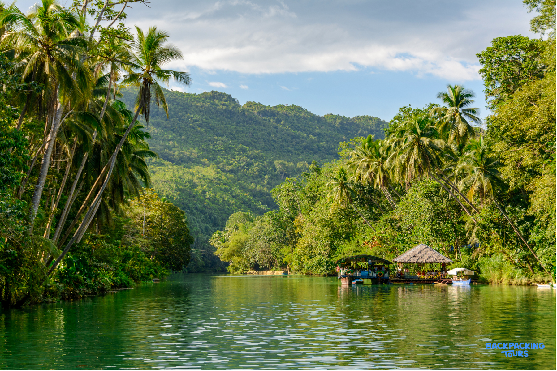 Lush tropical scenery along the Loboc River in Bohol, with a floating hut nestled among palm trees.