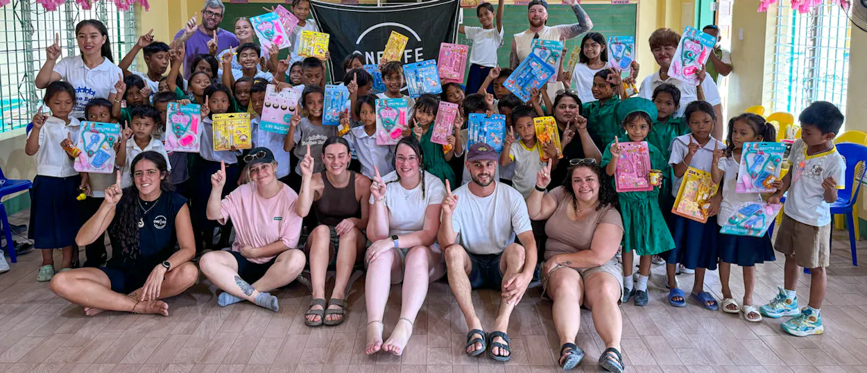 Backpackers and children smiling, holding gifts, and raising fingers during a school visit in Bohol.