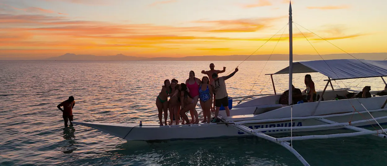 Happy travelers on an outrigger boat watch the beautiful sunset over calm waters in Bohol.