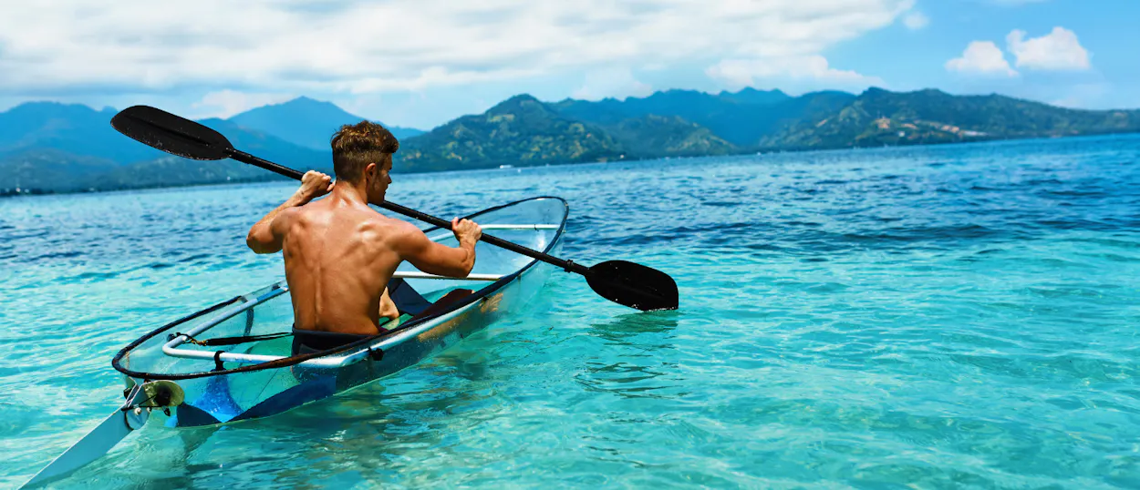 A man paddles a clear kayak in the turquoise waters of Boracay, looking at distant islands.