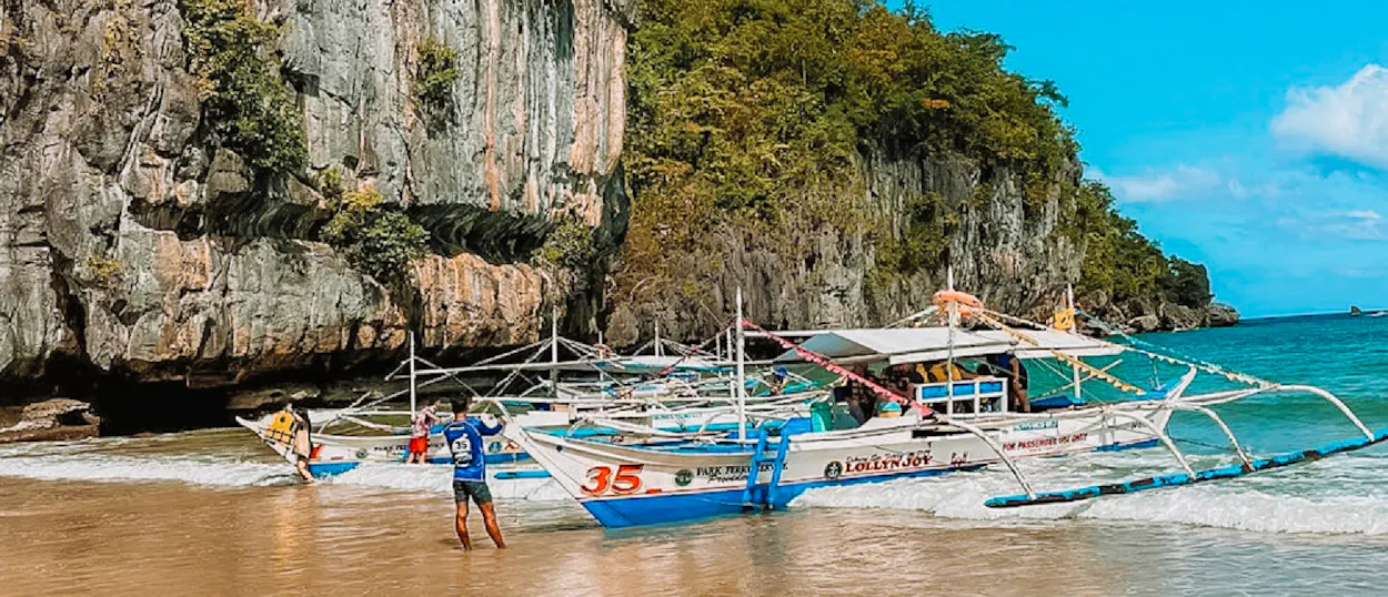Traditional bancas on a sandy beach with towering limestone cliffs and turquoise water in El Nido.