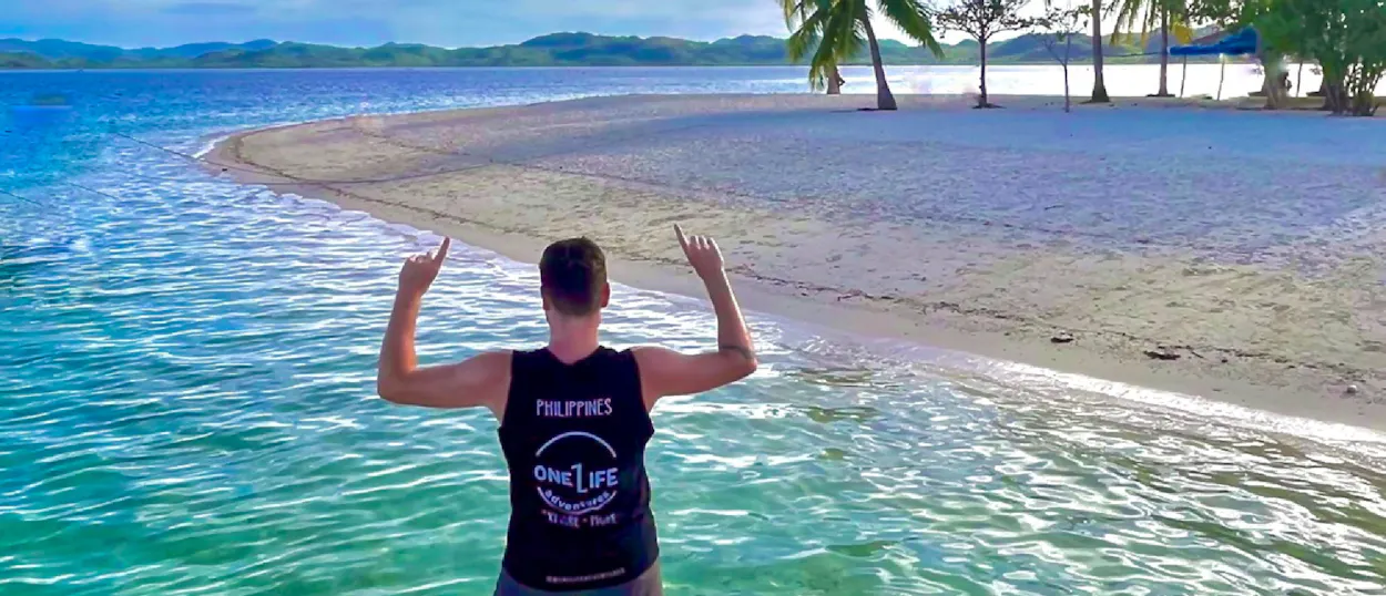 Person celebrating in clear turquoise water on a pristine white sand beach in Coron, Philippines.