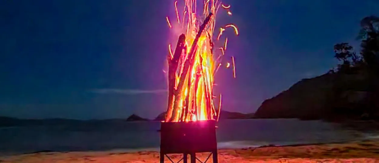 A large, crackling bonfire lights up a sandy beach at night on Island Camp, Philippines.